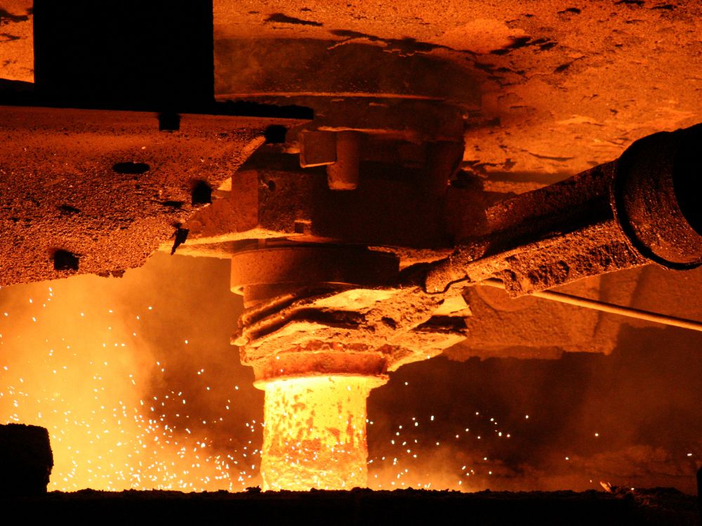 Processos de fundição com metal incandescente sendo vazado por equipamento industrial, mostrando etapa de fusão em alta temperatura.