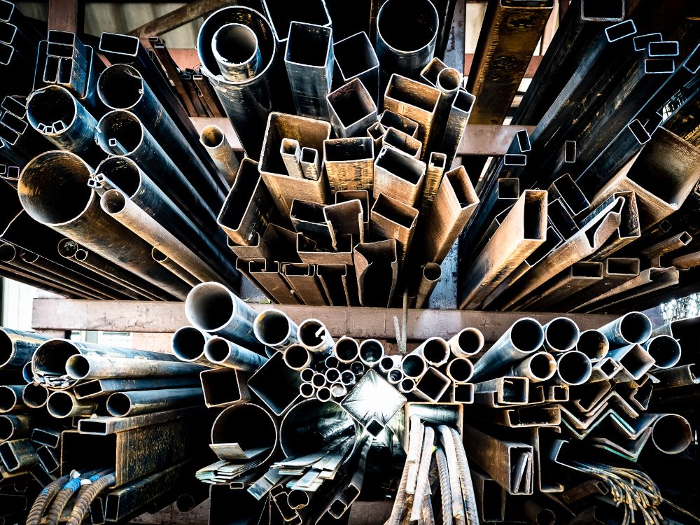 Estruturas metálicas com tubos e perfis variados armazenados em galpão industrial, representando os principais Tipos de ferro fundido usados em projetos industriais.