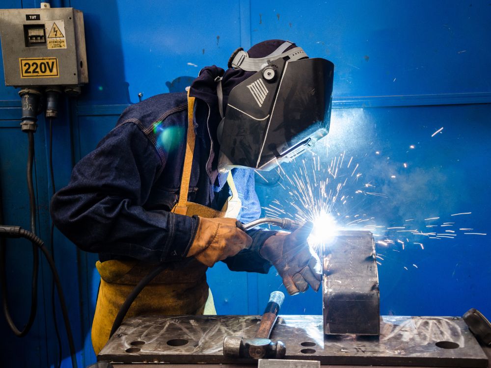Profissional realizando soldagem em peça metálica com equipamento de proteção, processo relacionado à manutenção e reparo de diferentes Tipos de ferro fundido.